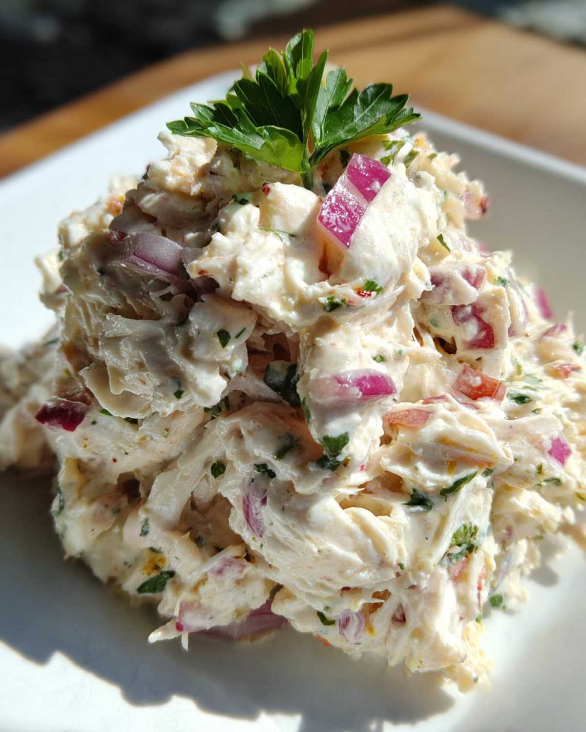 A mound of creamy crab salad mixed with visible chunks of red onion and topped with a parsley sprig.
