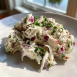 Close-up of creamy crab salad mixed with diced red onion and fresh parsley on a white plate.