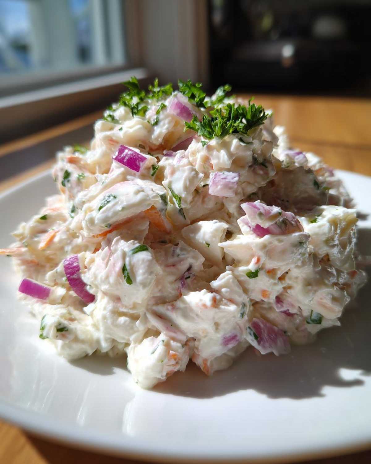 A mound of creamy crab salad mixed with diced red onion and herbs, garnished with fresh parsley on a white plate.