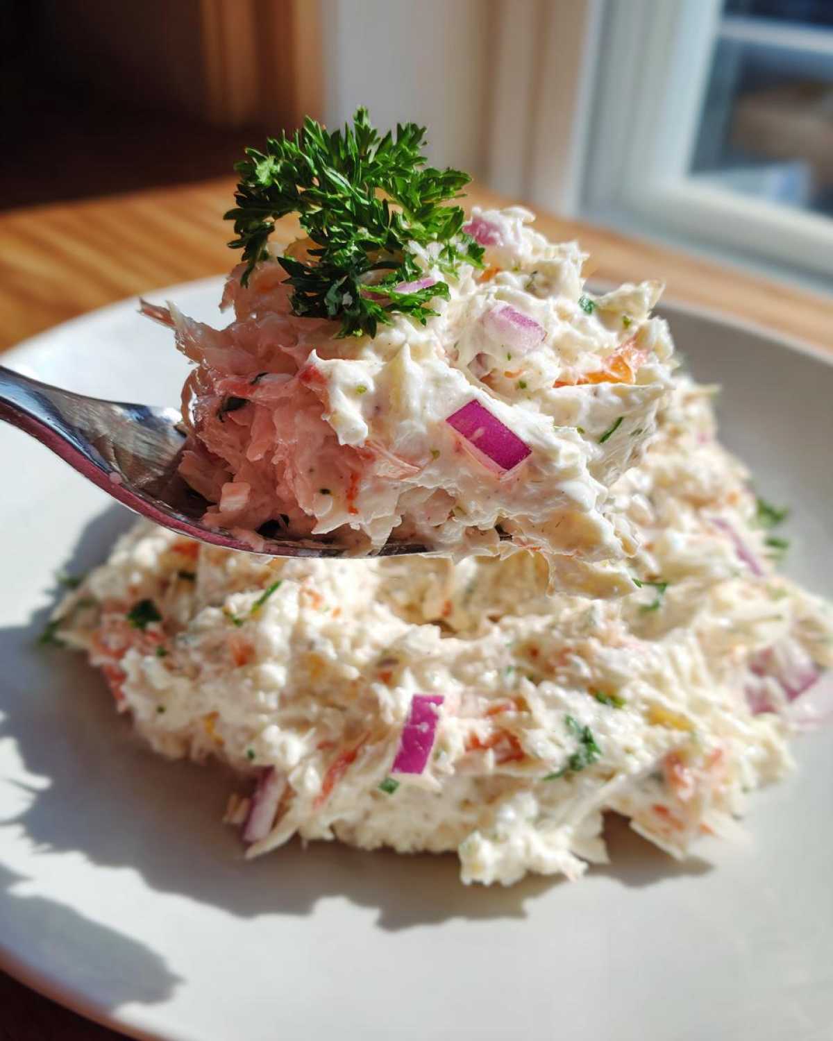 A spoonful of creamy crab salad featuring visible chunks of crab, red onion, and herbs, garnished with fresh parsley.