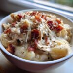 Close-up of a bowl filled with Creamy Crack Chicken Gnocchi topped with shredded cheese and crispy bacon bits.