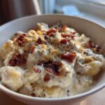 A close-up of a white bowl filled with Creamy Crack Chicken Gnocchi, topped generously with bacon bits and pepper.