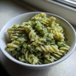 A close-up view of creamy Dill Pickle Pasta Salad featuring rotini pasta, chopped pickles, and fresh dill in a white bowl.