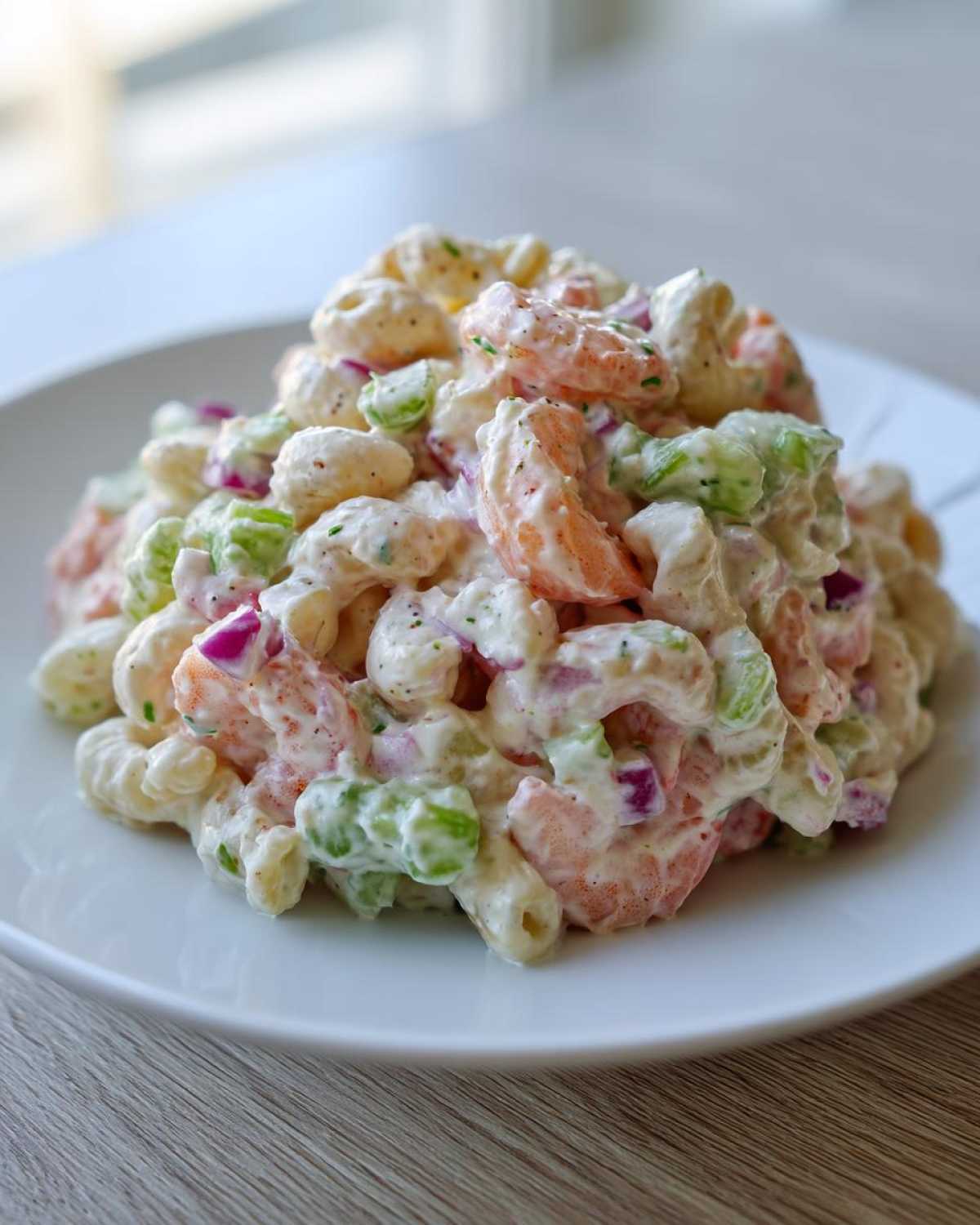 A generous serving of creamy Southern Shrimp Pasta Salad featuring elbow macaroni, pink shrimp, green celery, and red onion.