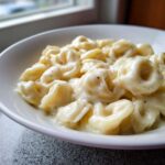 A close-up of a white bowl filled with creamy Tortellini Alfredo Recipe, lightly seasoned with pepper.