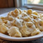 Close-up of a white bowl filled with cheesy Tortellini Alfredo Recipe, topped with cracked black pepper.