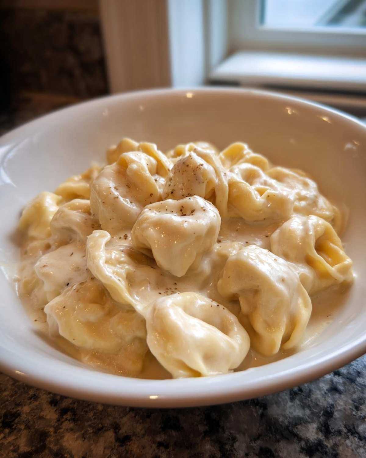 Close-up of cheesy tortellini coated in rich cream sauce, seasoned with black pepper, for the Tortellini Alfredo Recipe.