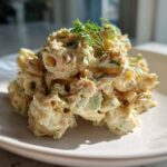 A mound of creamy tuna pasta salad, featuring elbow macaroni coated in a rich dressing and topped with fresh dill.