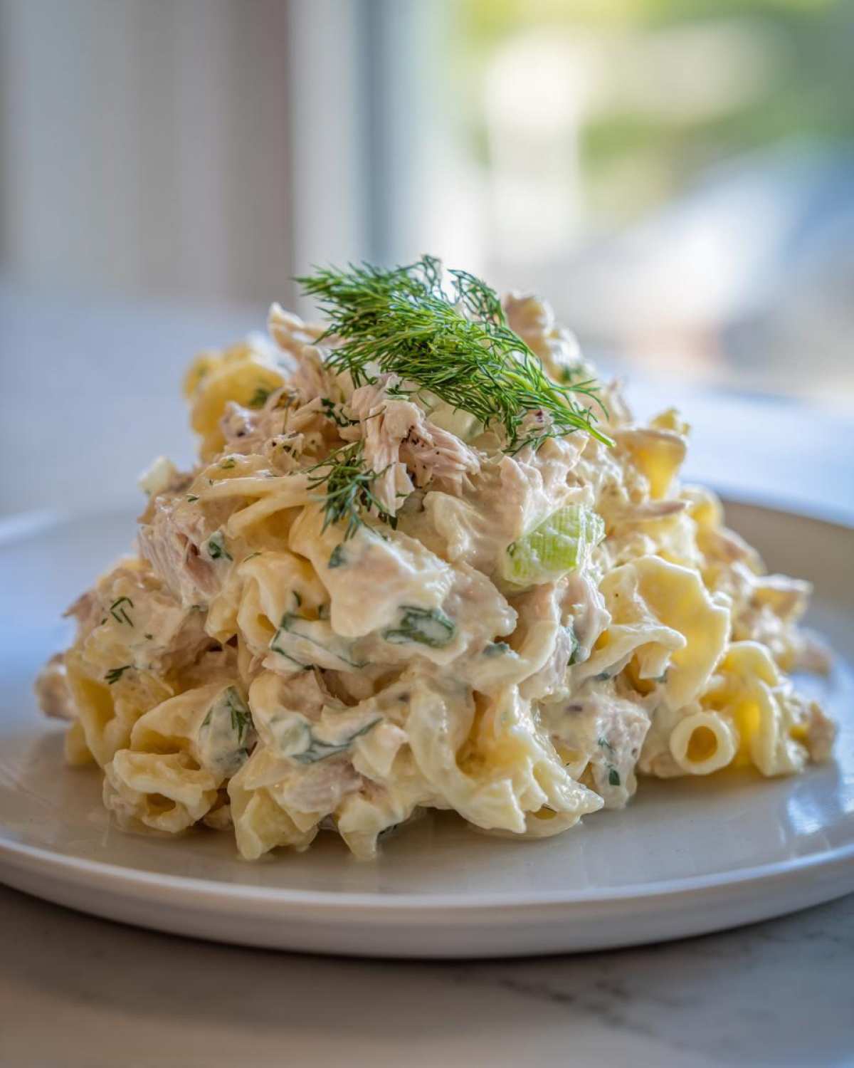 A mound of Creamy Tuna Pasta Salad featuring pasta, tuna, celery, and a creamy dressing, topped with fresh dill.