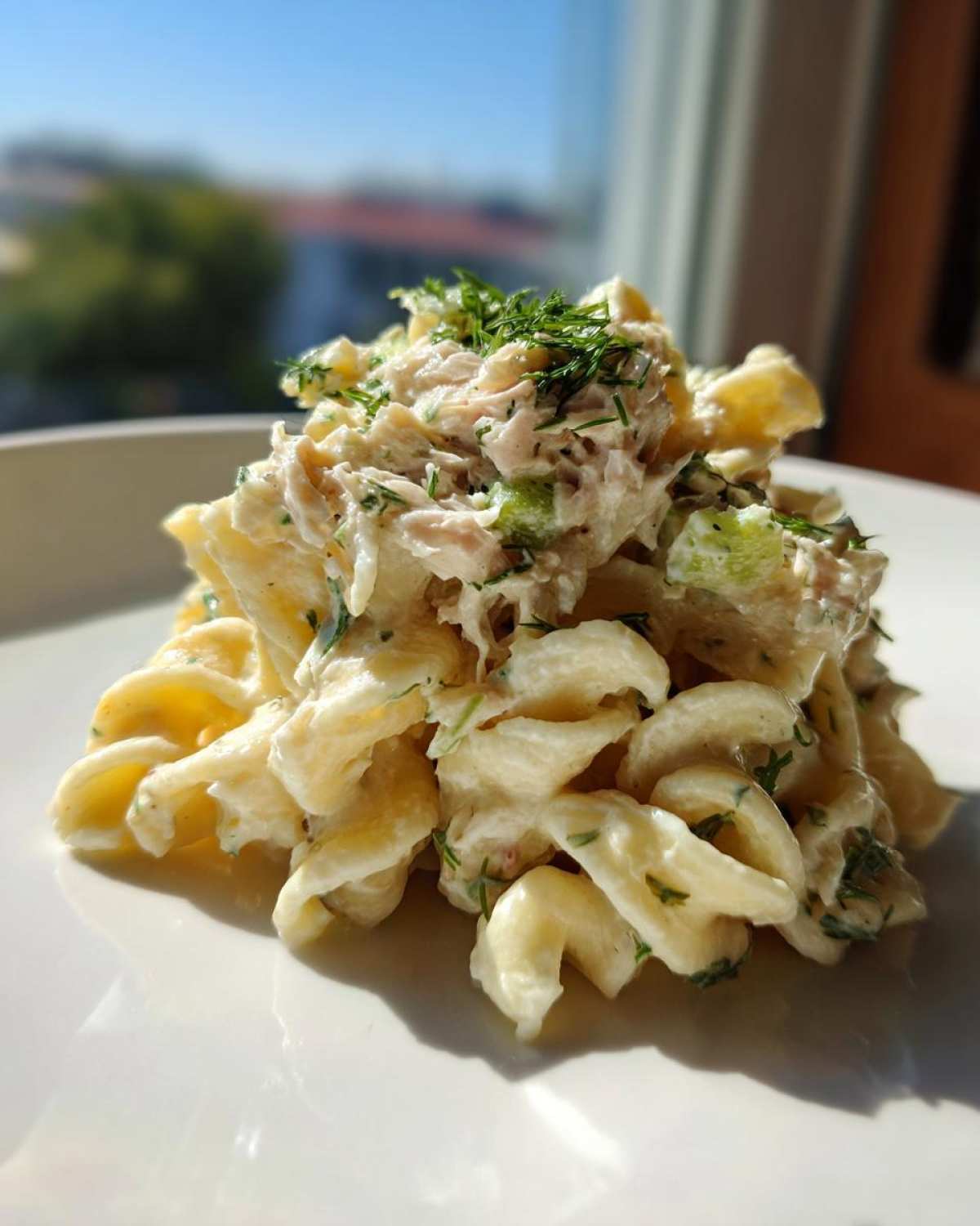 A close-up of a mound of Creamy Tuna Pasta Salad made with rotini pasta, topped with tuna mixture and fresh dill.