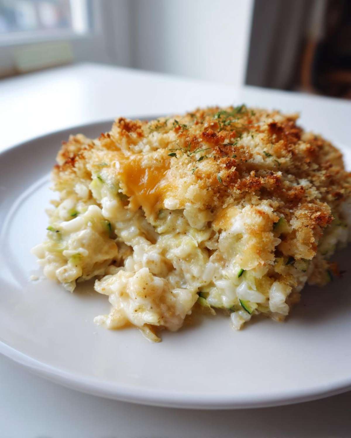 A generous serving of creamy Zucchini and Rice Casserole with a golden, crunchy breadcrumb topping.