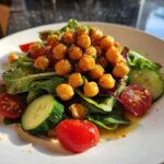 A vibrant plate featuring Crispy Air Fryer Chickpea Salad piled high with seasoned chickpeas, mixed greens, cucumber slices, and cherry tomatoes.
