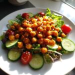 A vibrant salad topped with a generous mound of Crispy Air Fryer Chickpea Salad, surrounded by cucumber slices and cherry tomatoes.