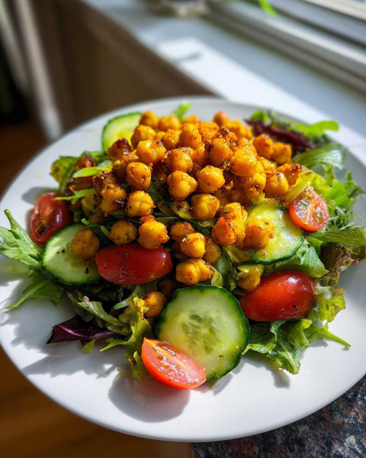 A vibrant plate of Crispy Air Fryer Chickpea Salad topped with seasoned chickpeas, cucumber slices, and cherry tomatoes.