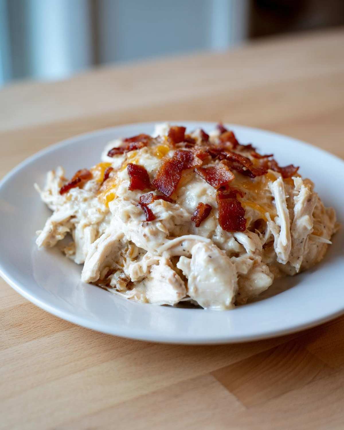 A serving of creamy Crockpot Crack Chicken (Bacon Cheddar Ranch) topped with crispy bacon bits on a white plate.