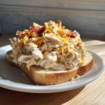 A thick serving of creamy Crockpot Crack Chicken (Bacon Cheddar Ranch) piled high on a slice of toasted white bread.