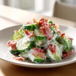 A mound of creamy Cucumber Bacon Ranch Salad featuring sliced cucumbers tossed in ranch dressing and topped with crispy bacon pieces.