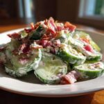 A close-up of fresh Cucumber Bacon Ranch Salad featuring creamy dressing and crispy bacon crumbles on a white plate.