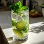 A tall glass filled with effervescent Cucumber Mint Sparkling Lemonade, featuring cucumber slices and mint leaves.