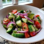 Close-up of a vibrant Cucumber Onion Tomato Salad with chunks of cucumber, red onion slices, and halved cherry tomatoes.