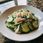 A white bowl filled with refreshing Cucumber Salad with Crab Meat Seafood Feast, featuring sliced cucumbers and shredded crab.