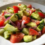 A vibrant close-up of the Cucumber Tomato Avocado Salad featuring chunks of cucumber, tomato, avocado, and red onion.