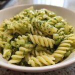 Close-up of creamy Dill Pickle Pasta Salad featuring fusilli pasta, chopped pickles, and fresh dill in a white bowl.