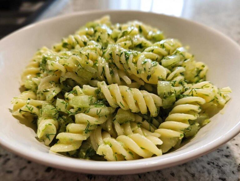 Close-up of creamy Dill Pickle Pasta Salad featuring fusilli pasta, chopped pickles, and fresh dill in a white bowl.