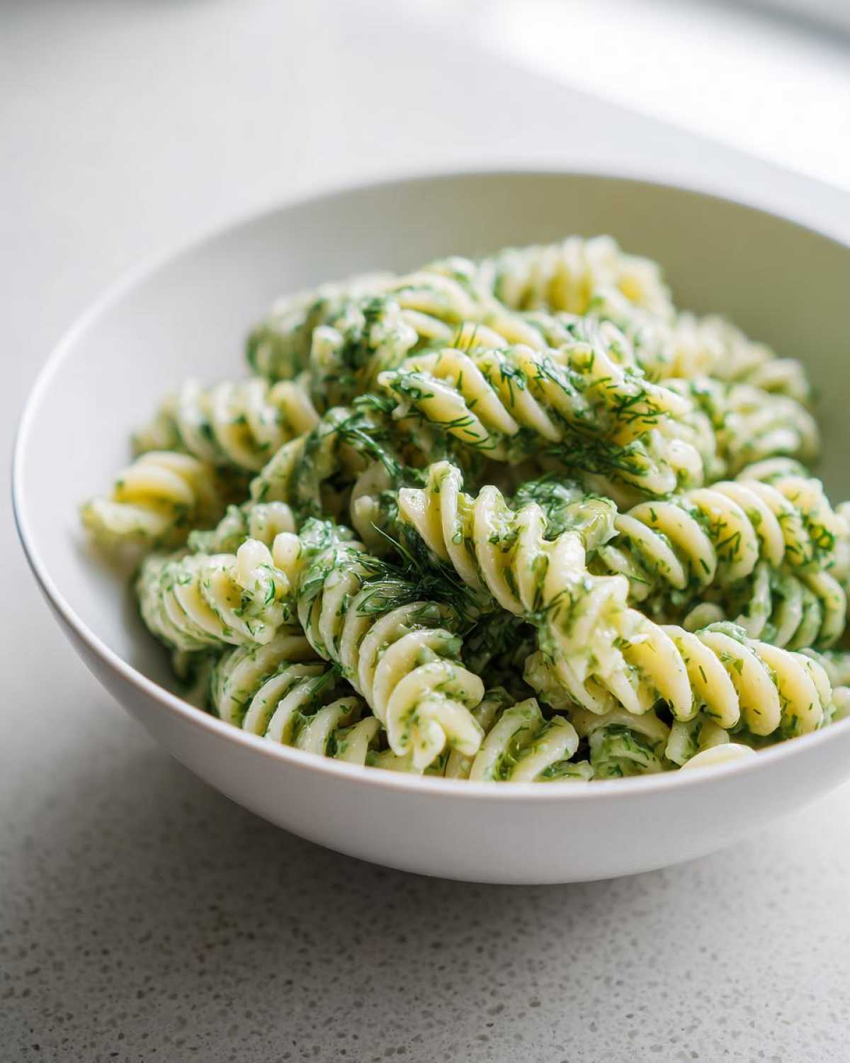 Close-up of creamy Dill Pickle Pasta Salad made with fusilli pasta coated in a green, herby sauce.