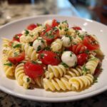 Close-up of a bowl of Easy Caprese Pasta Salad featuring fusilli pasta, cherry tomatoes, and small mozzarella balls.