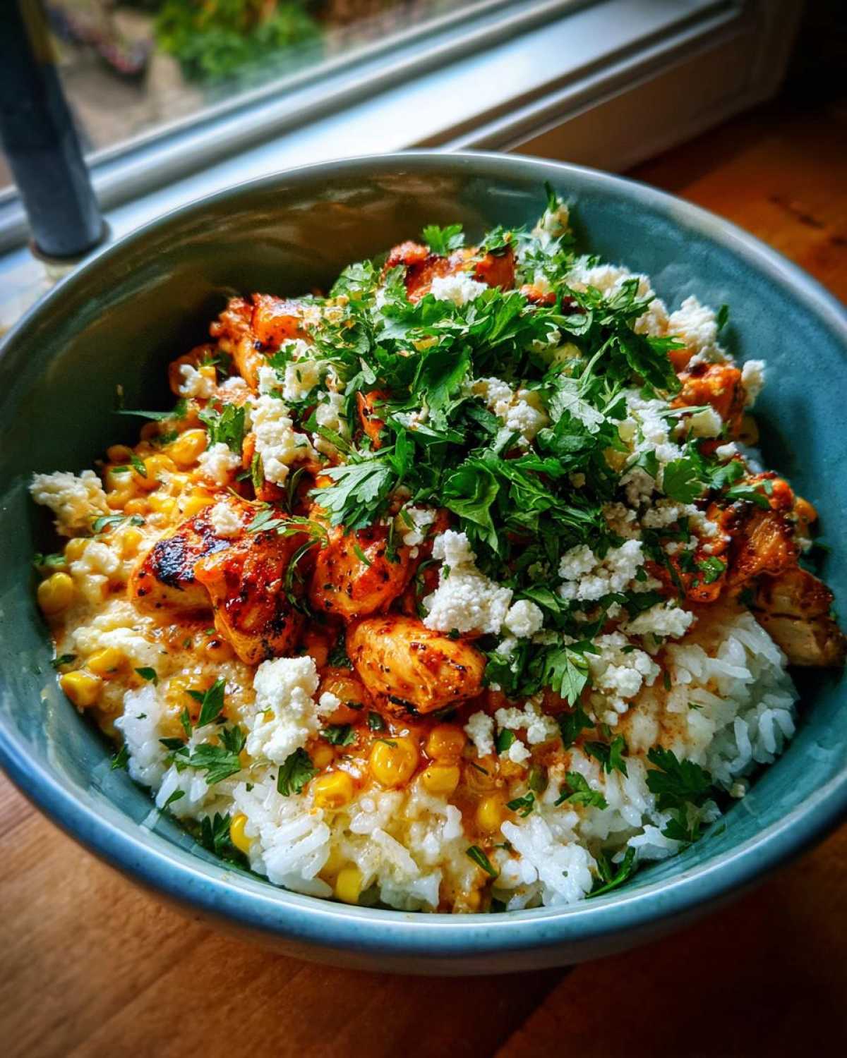 Close-up of an Easy Street Corn Chicken Rice Bowl with seasoned chicken, corn, white rice, crumbled white cheese, and fresh parsley.