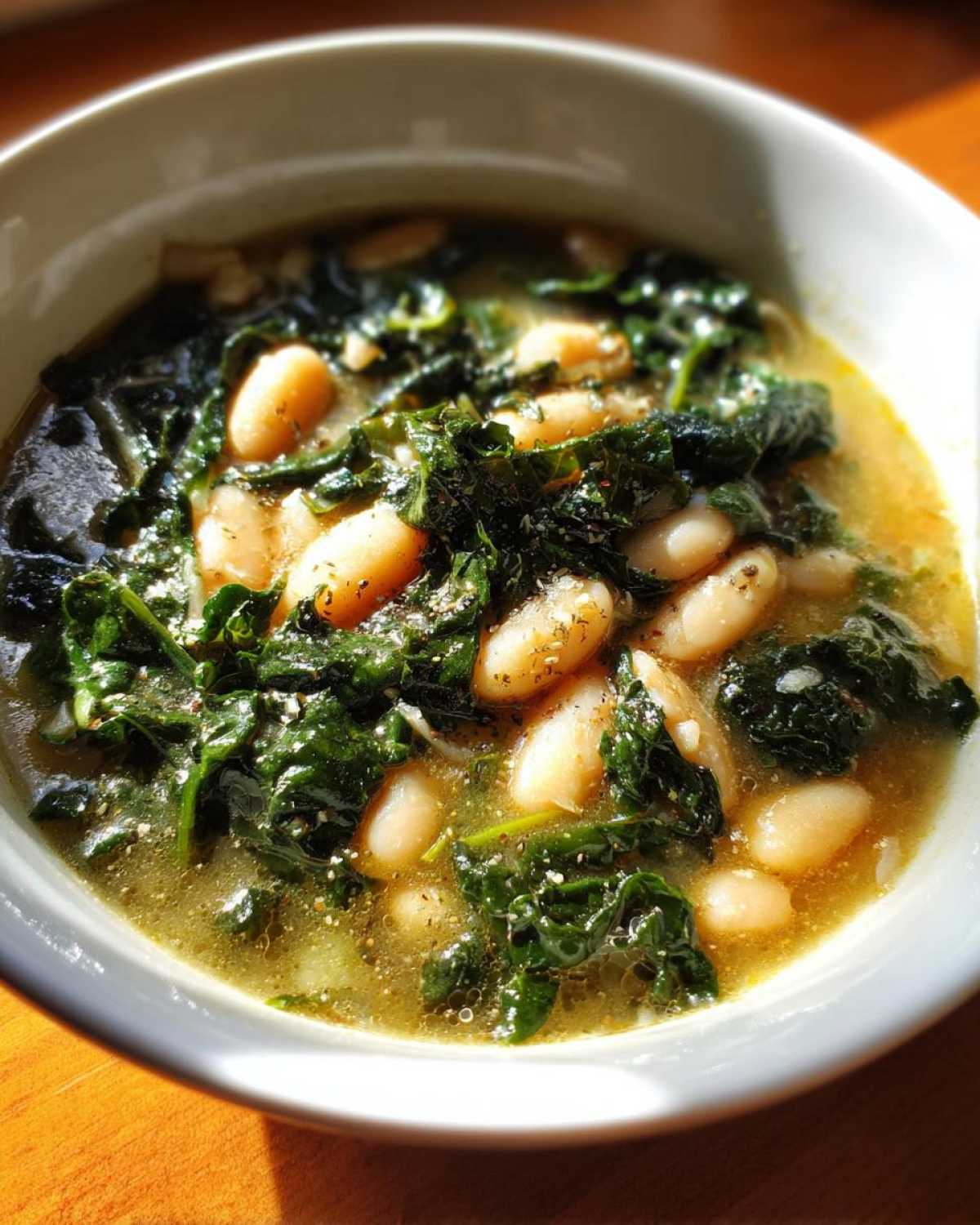 A close-up bowl of Easy Tuscan White Bean Soup featuring creamy white beans and dark green wilted kale in a savory broth.