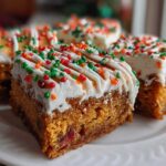 Close-up of several rich, orange-hued cranberry bliss bars topped with white frosting and festive red, green, and orange sprinkles.