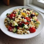 A close-up of a serving of Feta Mediterranean Pasta Salad featuring pasta, cherry tomatoes, cucumber, feta cheese, and Kalamata olives.