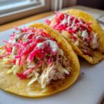 Two appetizing Fish Tacos with Rhubarb Pineapple Salsa, featuring shredded fish, slaw, and white crema drizzle.