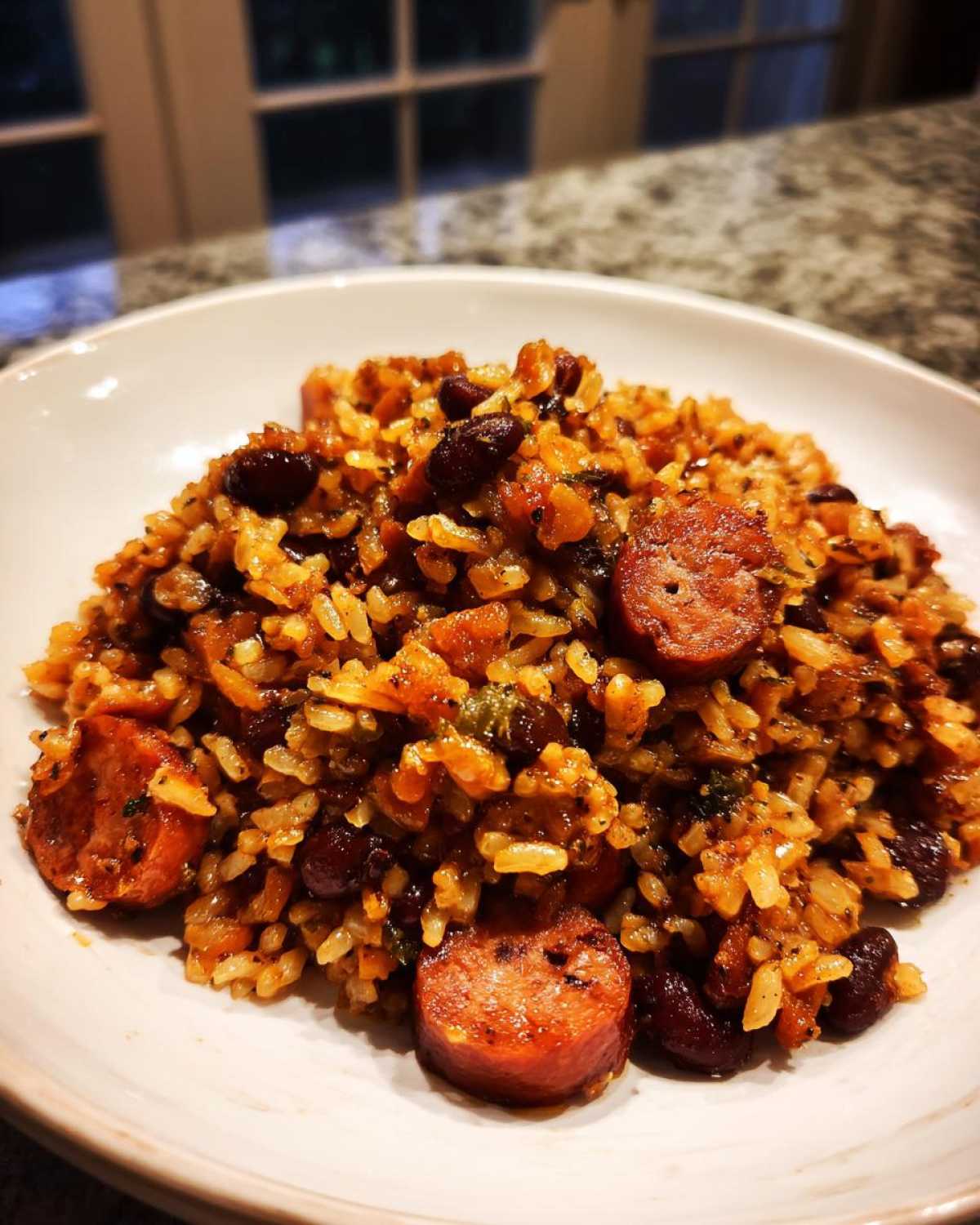 Close-up of a white bowl filled with seasoned beans and rice mixed with slices of smoked sausage.