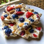 Stacked pieces of Frozen Yogurt Bark with Fruit & Nuts topped with blueberries, strawberries, and sliced almonds.