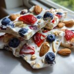 Close-up of stacked pieces of Frozen Yogurt Bark with Fruit & Nuts, topped with blueberries, strawberries, and almonds.