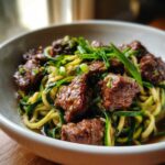 A bowl of Garlic Butter Steak Bites with Zucchini Noodles, garnished with fresh green onions.
