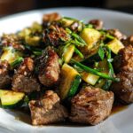 Close-up of savory Garlic Butter Steak Bites mixed with sautéed zucchini noodles on a white plate.
