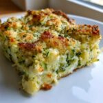 A close-up of a square slice of Garlic Parmesan Zucchini Casserole with a golden, crunchy topping.