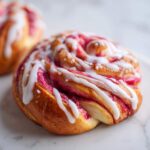 A close-up of a freshly baked Geometric Rhubarb Cardamom Bun topped with white icing drizzle and coarse sugar.