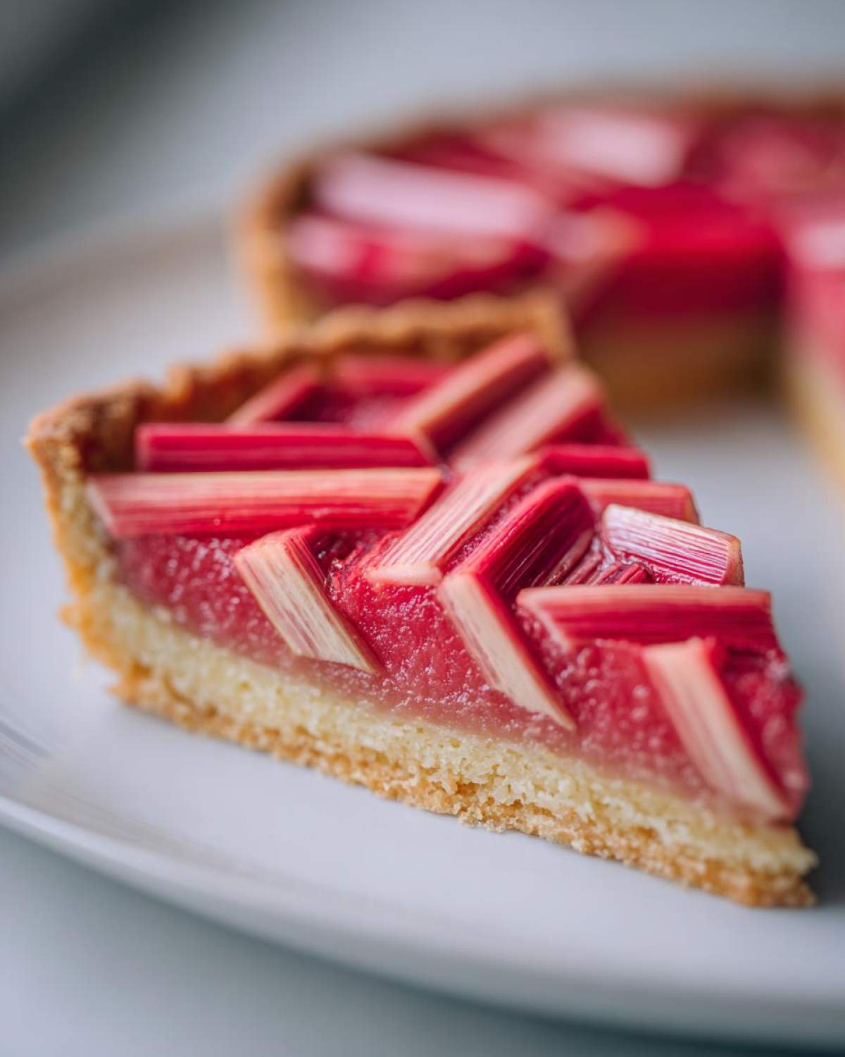 Close-up of a slice of Geometric Rhubarb Tart showing the geometric rhubarb topping over frangipane and a crisp crust.