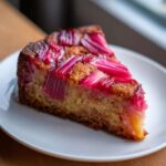 A close-up slice of Geometric Rhubarb Upside-Down Spice Cake showing bright pink rhubarb pieces on a golden, spiced crumb.