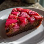 A close-up slice of Geometric Rhubarb Upside-Down Spice Cake featuring bright pink rhubarb arranged on a dark, moist spice cake base.
