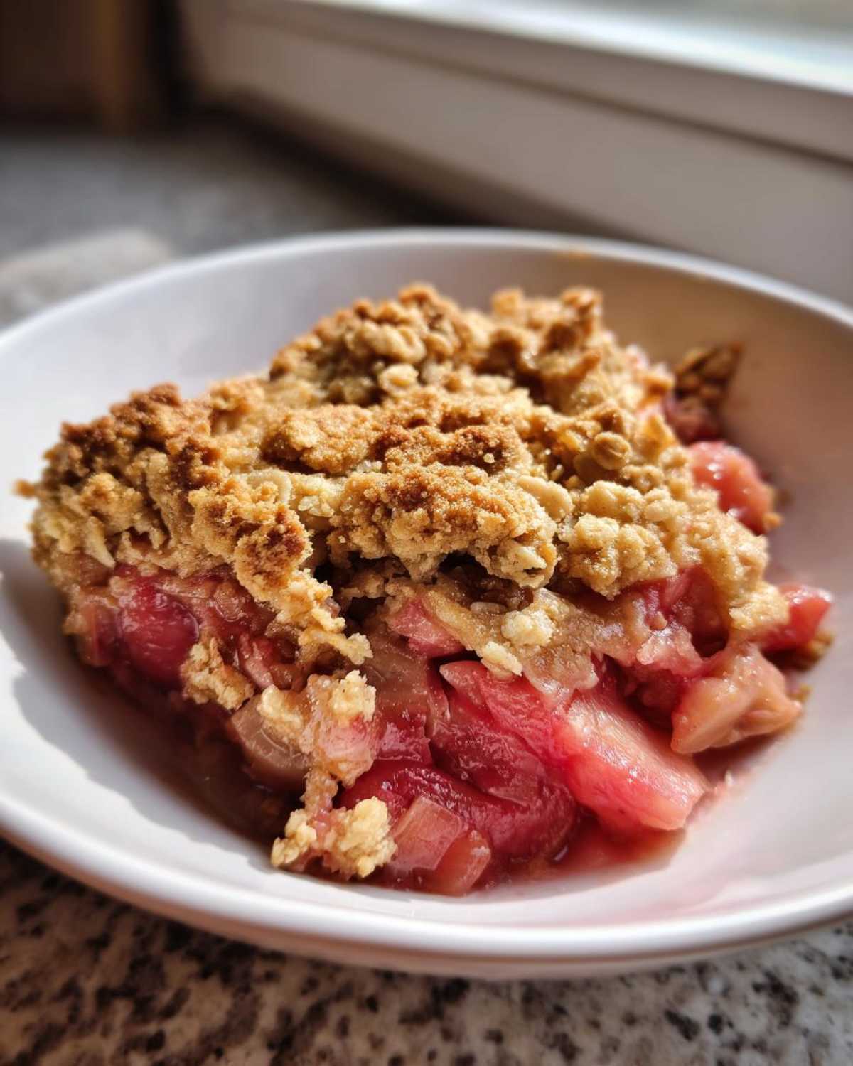 A close-up serving of Gluten-Free Rhubarb Crisp showing bright pink rhubarb filling and a golden, crumbly oat topping in a white bowl.