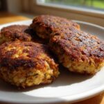 Four perfectly seared Homemade Salmon Patties resting on a white plate, catching bright sunlight.