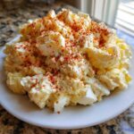A mound of creamy Grandma's Old-Fashioned Potato Salad topped generously with paprika on a white plate.