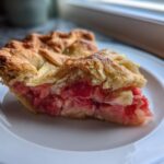 Close-up of a slice of Grandma's Rhubarb Pie with Lard Crust showing flaky golden top and bright pink filling.