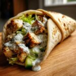 Close-up of a Greek Chicken Wrap filled with seasoned chicken, lettuce, and drizzled generously with garlic yogurt sauce.